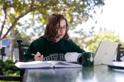 A student seated at a table outside reviews information on her laptop